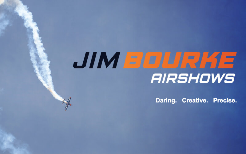 An airplane leaving a smoke trail against the sky with the Jim Bourke Airshows logo